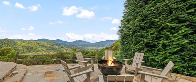 Outdoor patio with Adirondack chairs, fire pit, and mountain valley views beyond ivy-covered wall